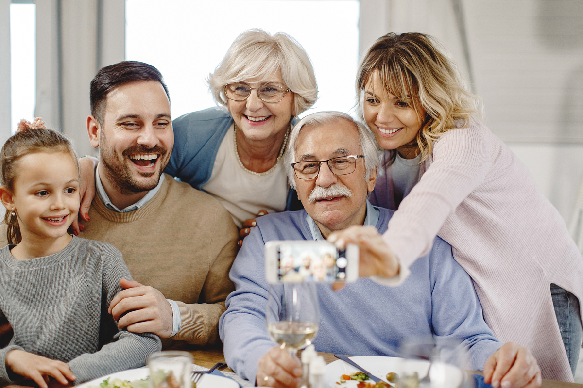 Happy extended family using smart phone taking selfie in dining room.
